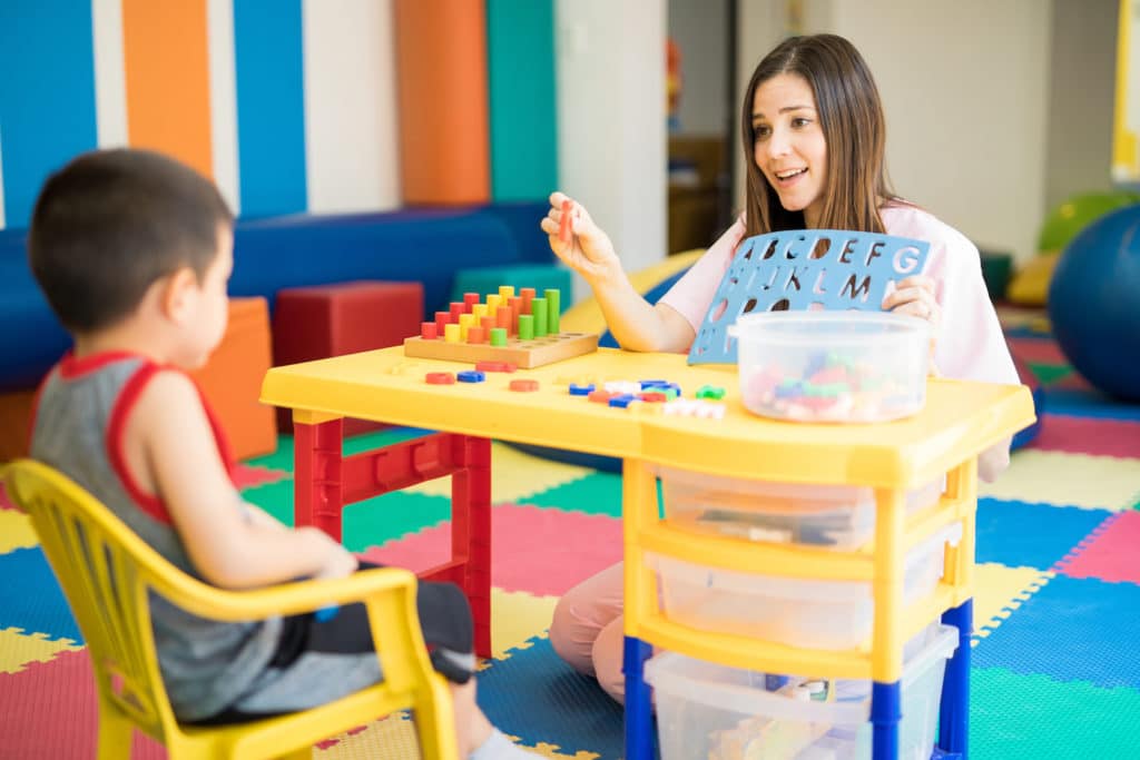 Teacher working with a young boy teaching him letters.
