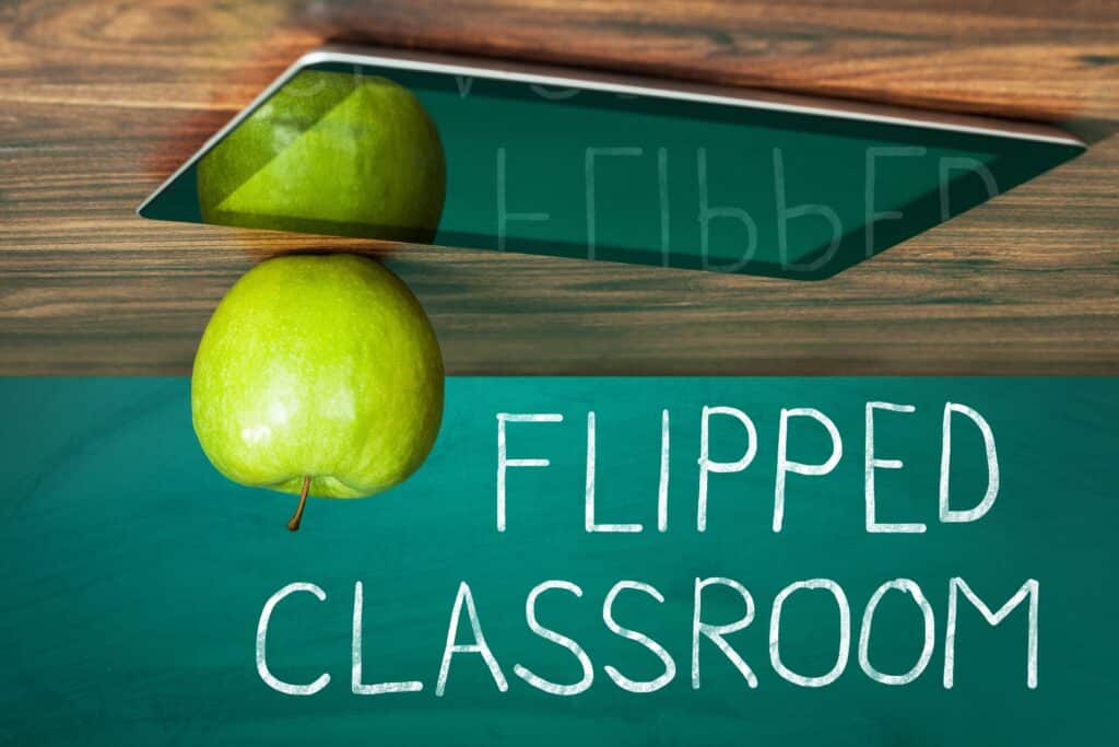 A portrait of an upside-down apple sitting on a tablet with the text “flipped classroom.”