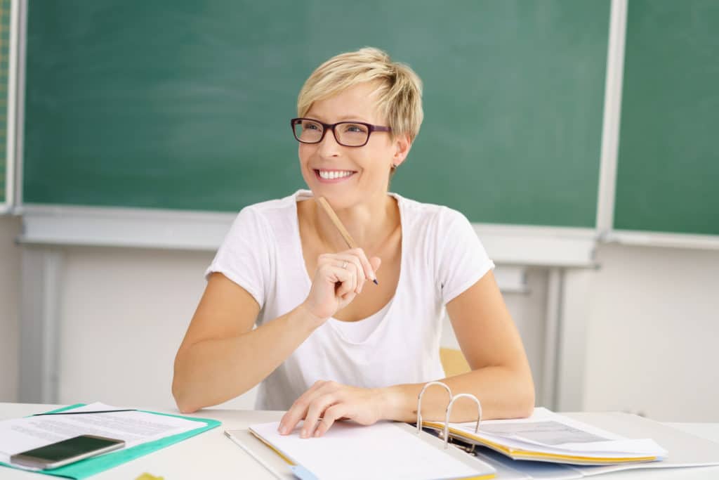 Female teacher thinking at her desk while working on paperwork.