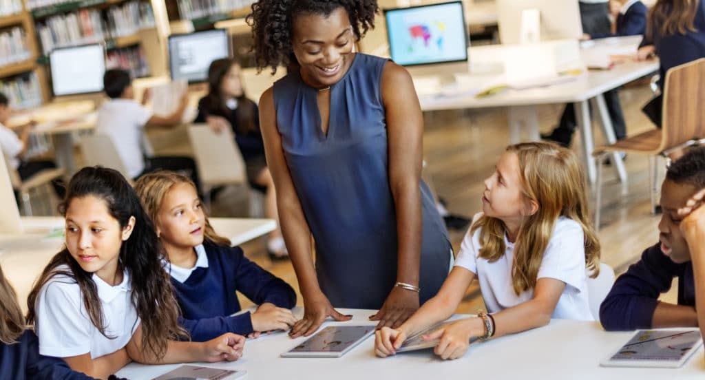 Teacher standing next to a group of students working in the library.