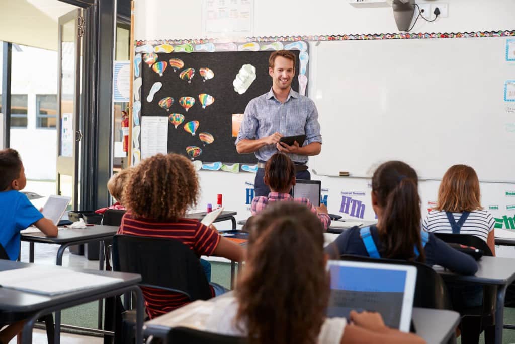 Teacher standing at the front of a classroom talking to students.