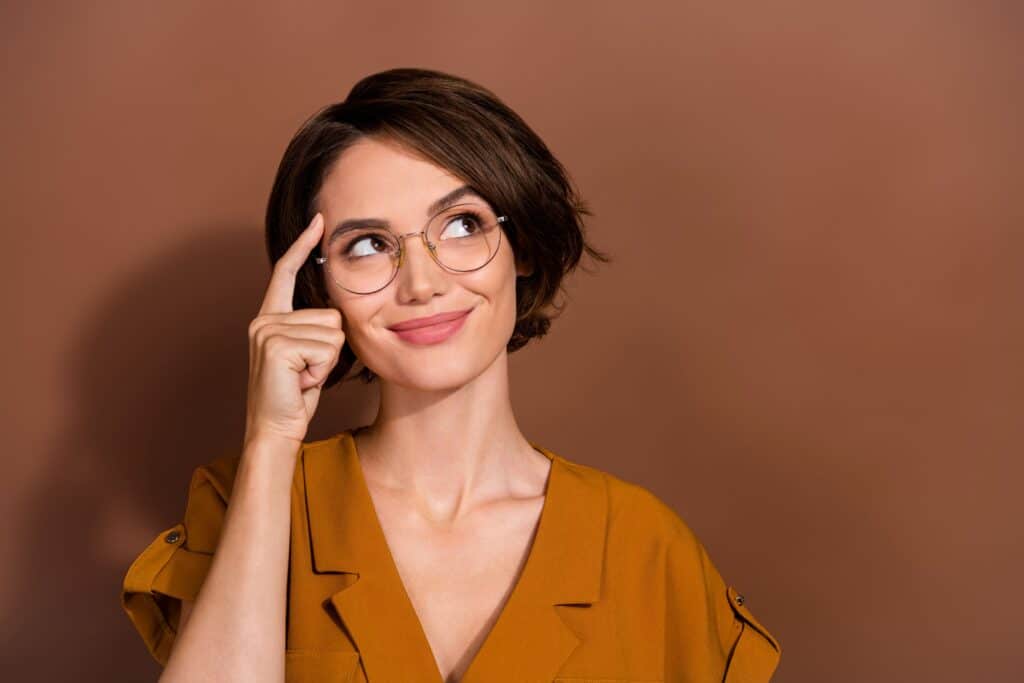 A woman holds a finger up to her forehead in a thinking motion.
