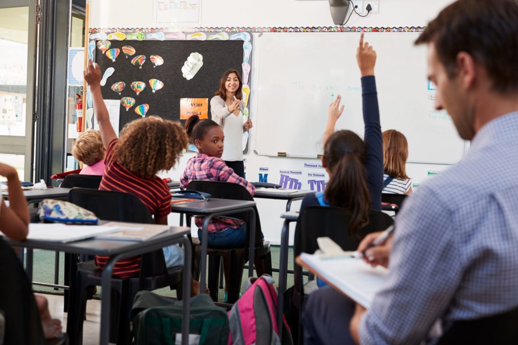 A teacher stands at the front of a classroom, teaching a lesson during her classroom observation.