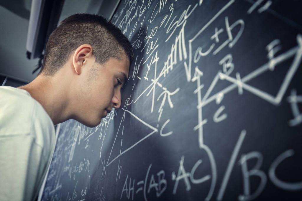 Frustrated student with his head against a blackboard with math equations written on it.