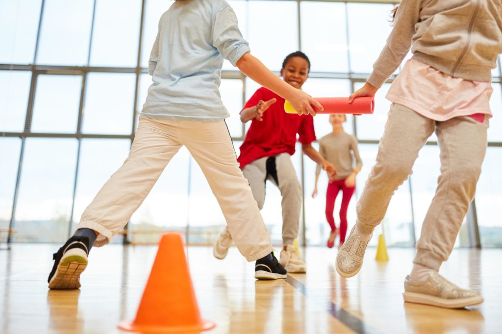 Group of young children having a relay race in gym class.