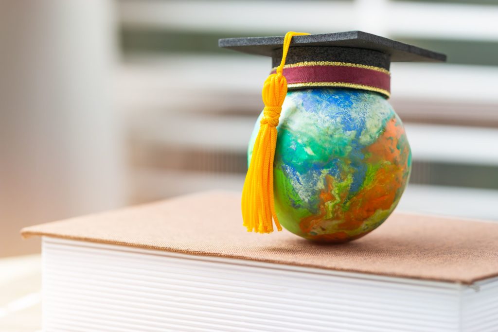 A graduation cap sits on top of a small globe, which is balanced on a textbook.