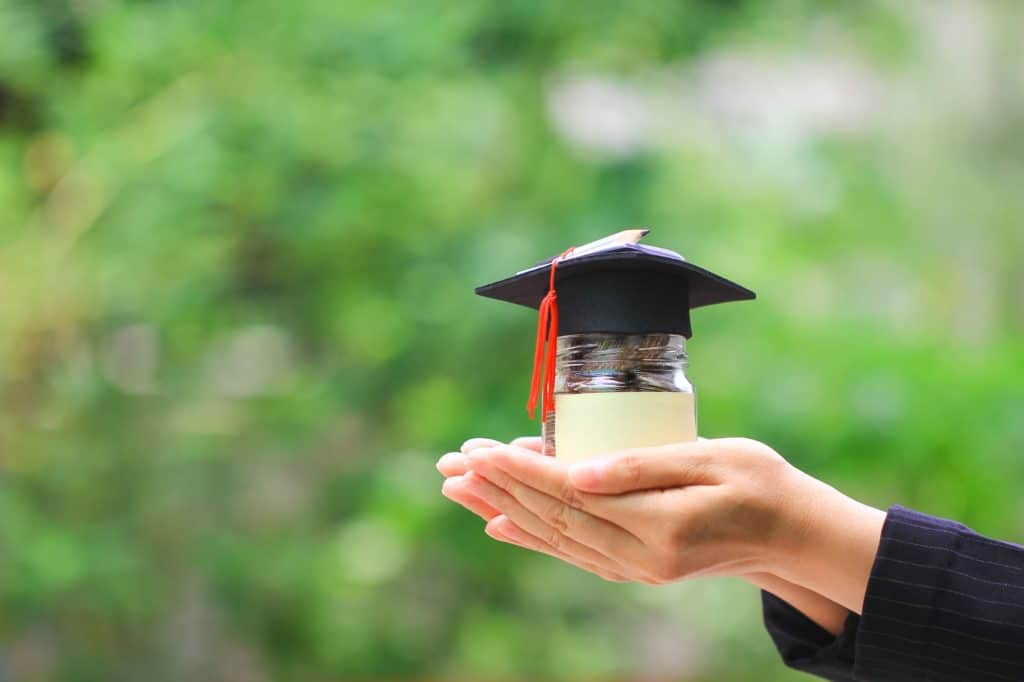 Graduate holding jar of coins with graduation cap on top
