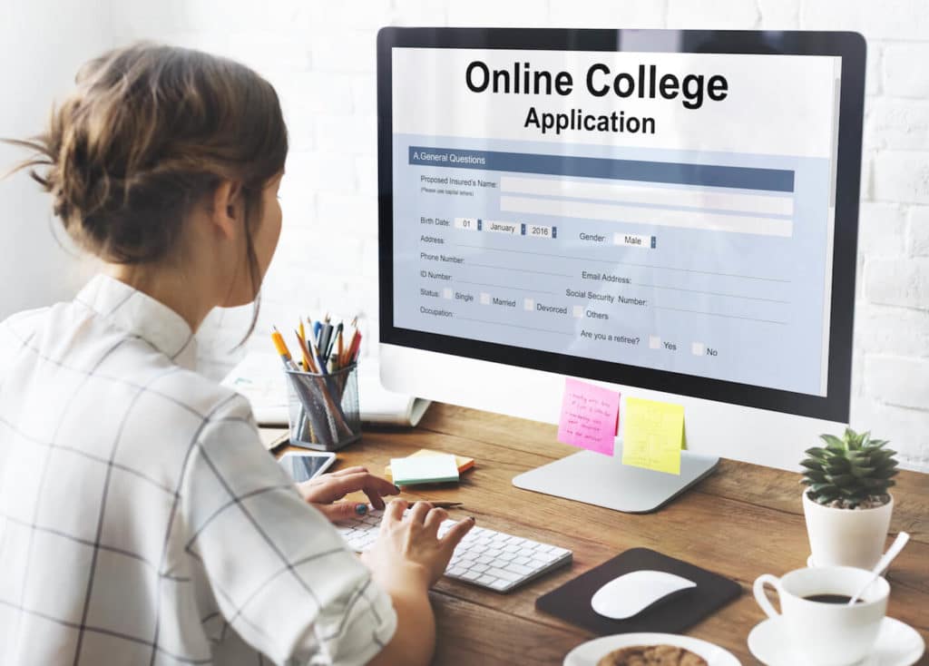 Woman sitting at a desk with a computer, filling out an online college application.