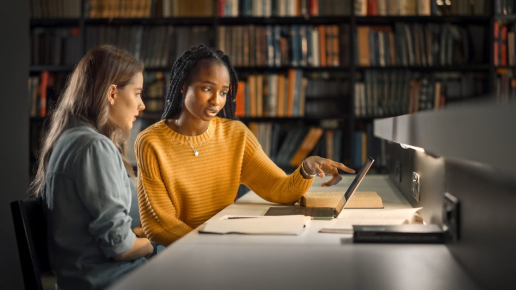 Two gifted students work on a project together on a laptop in a school library.