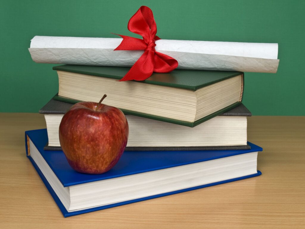 A certificate sits on top of a stack of books and next to an apple.