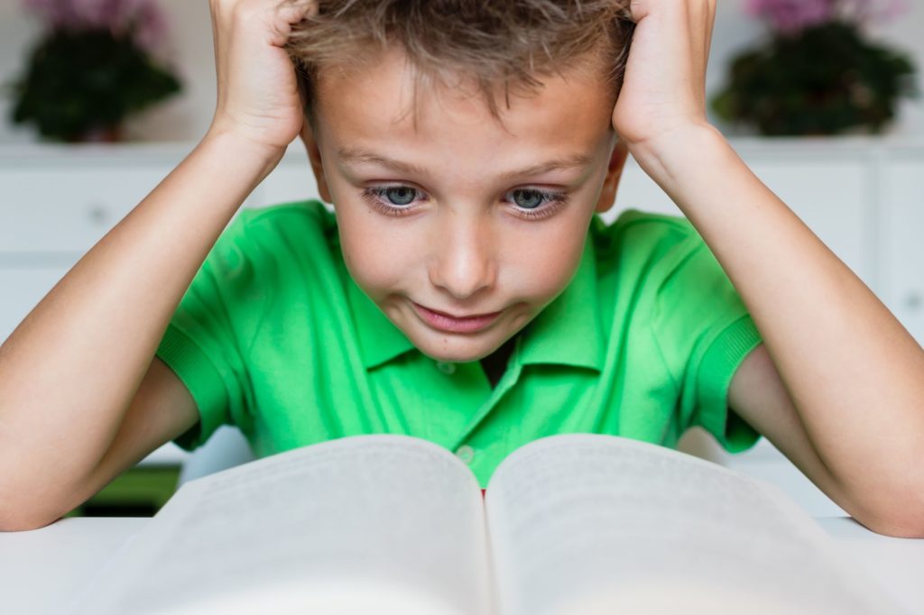 Young boy looking frustrated while reading a book.