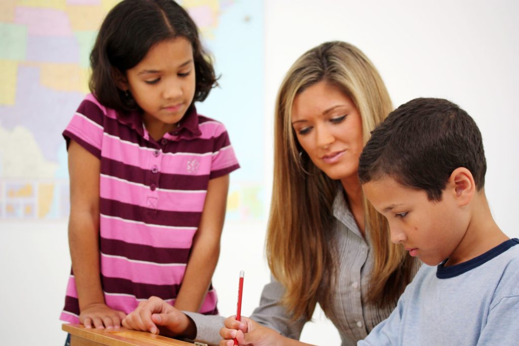 Teacher working with two young Hispanic students in a classroom.