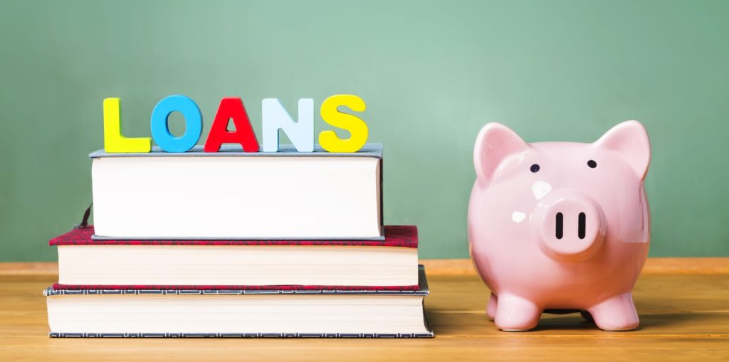 Letters spelling ‘loans’ on top of a stack of books next to a piggy bank.