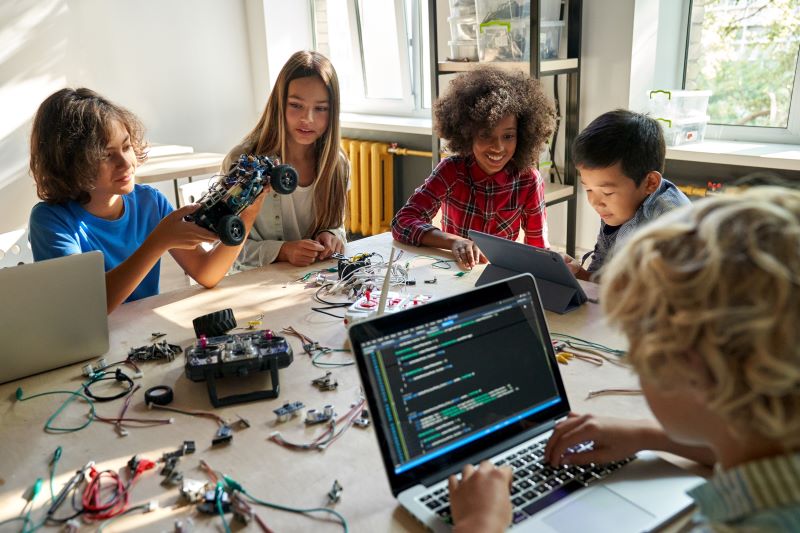 A group of middle school students build robotic cars using computers and coding.