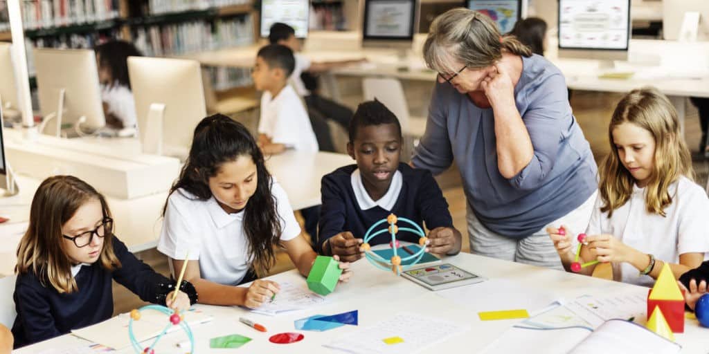 Group of students working at a table with a teacher standing near by.