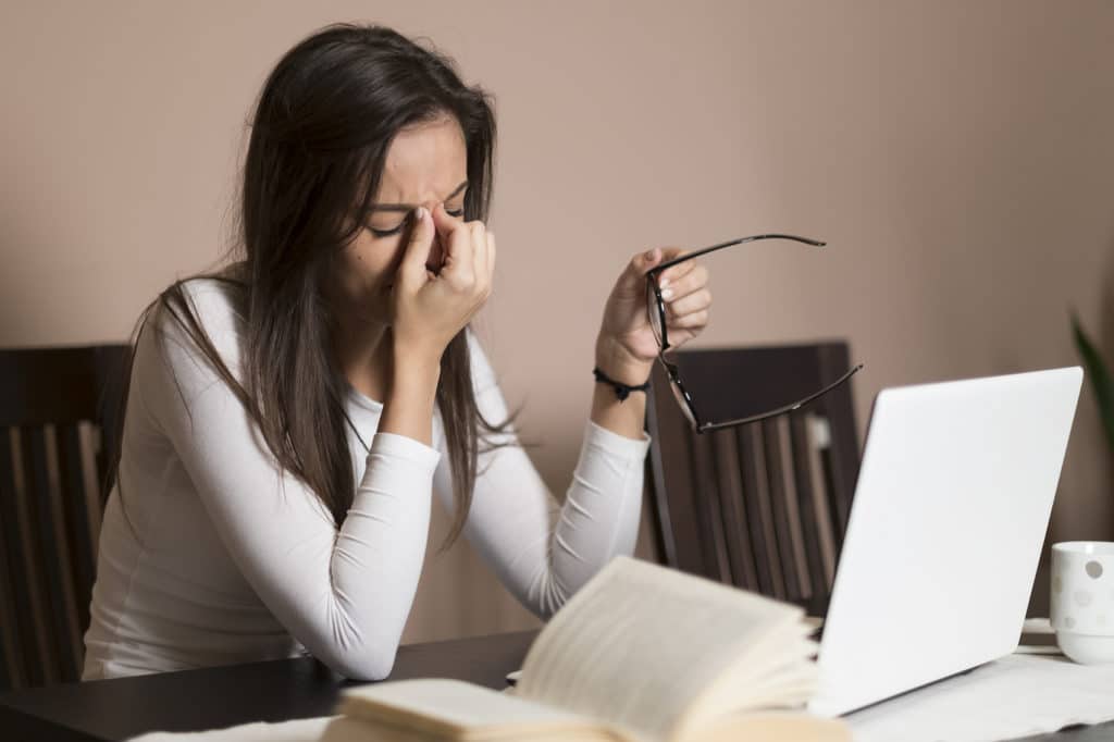 Frustrated young women pinching her furrowed brow while using a laptop.