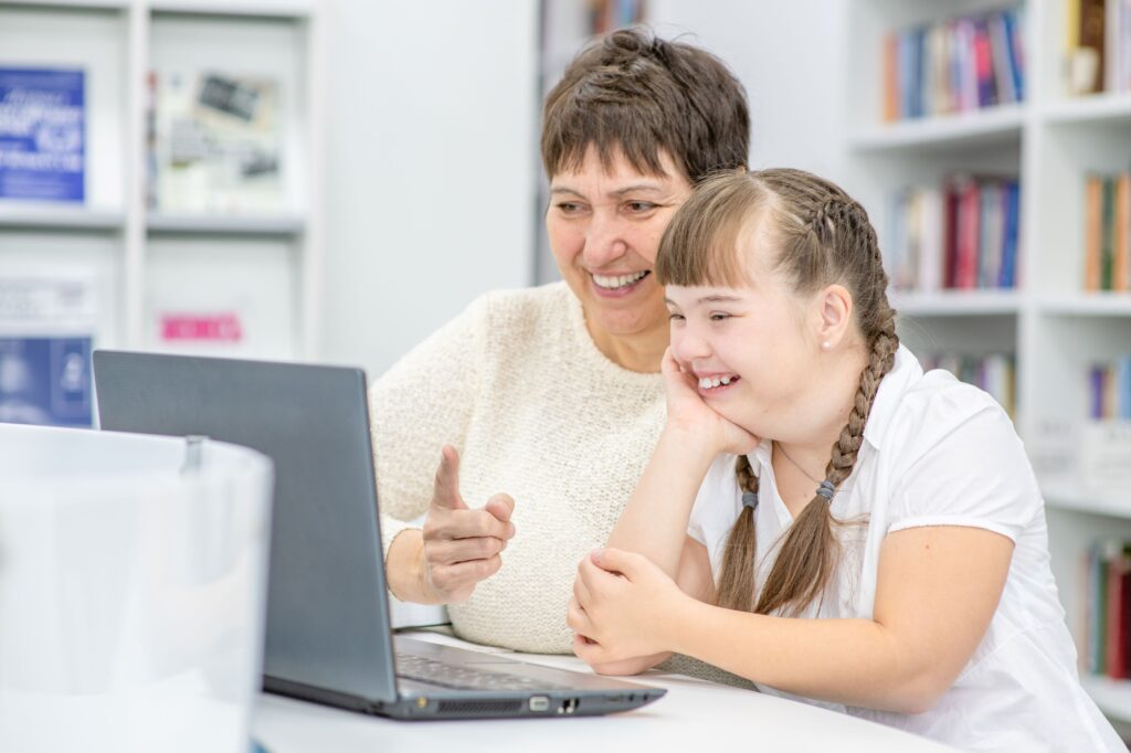 A teacher assists a special education student in using her laptop for a lesson.