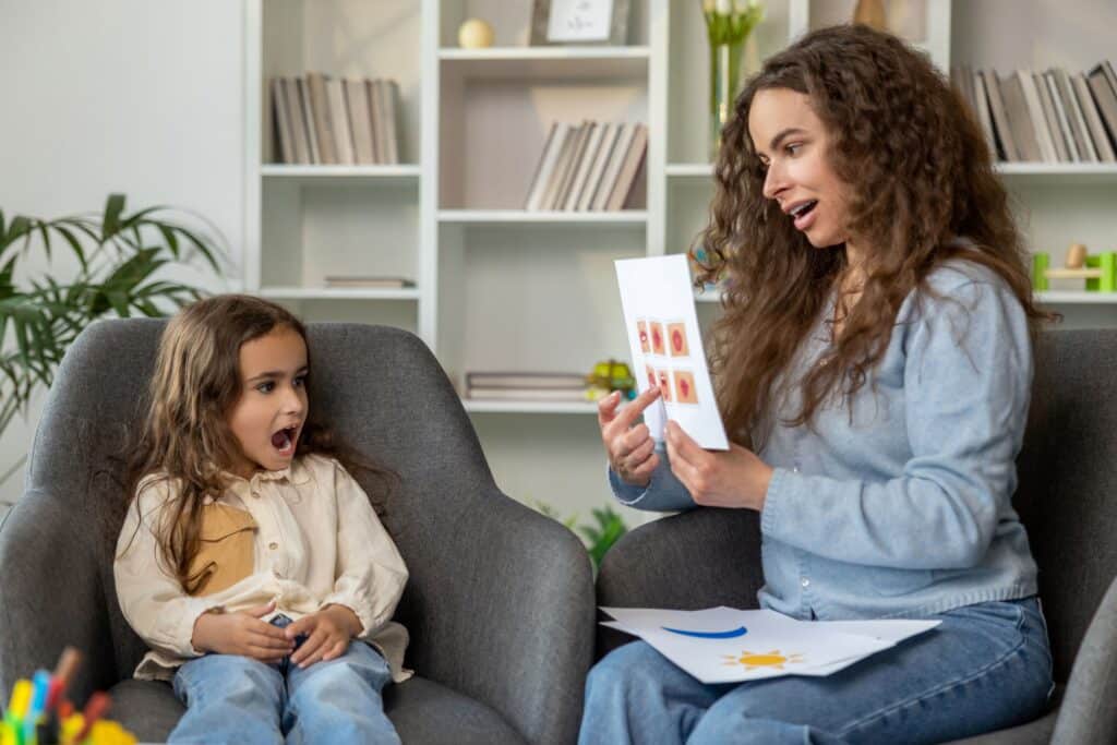 How to become a speech-language pathologist: a SLP sits with a student, helping her pronounce words with cue cards.
