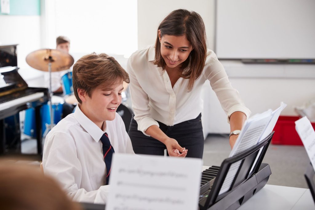 A student plays piano while his music teacher helps him.