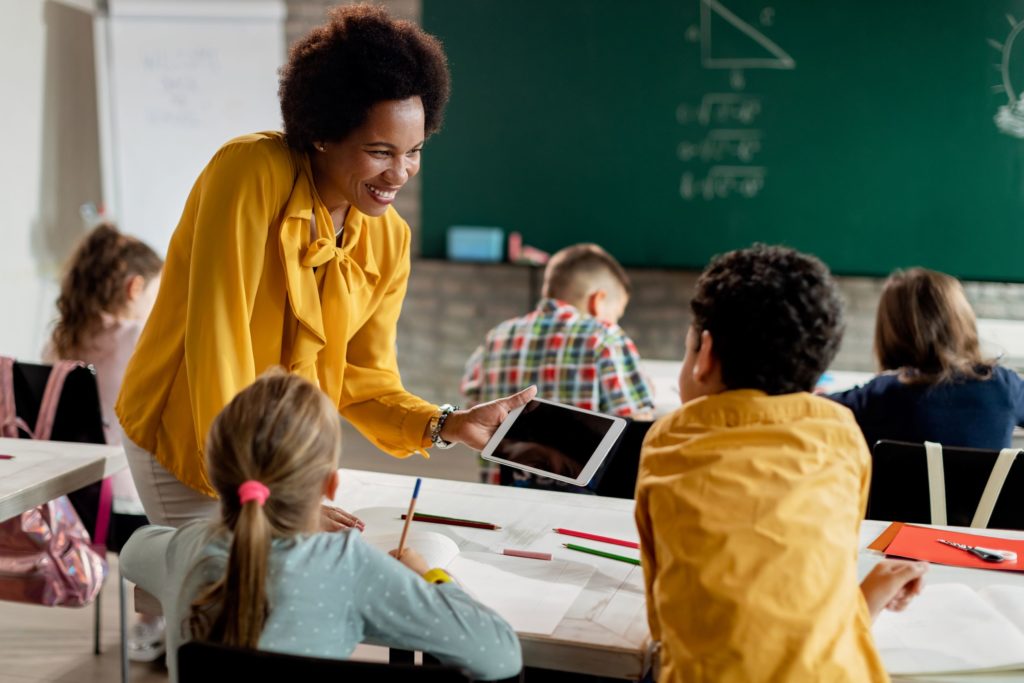 A teacher helps her student by showing him something on a tablet.