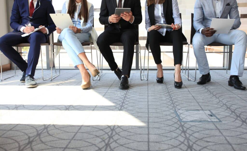 A group of people sit outside of a job interview, waiting their turn.
