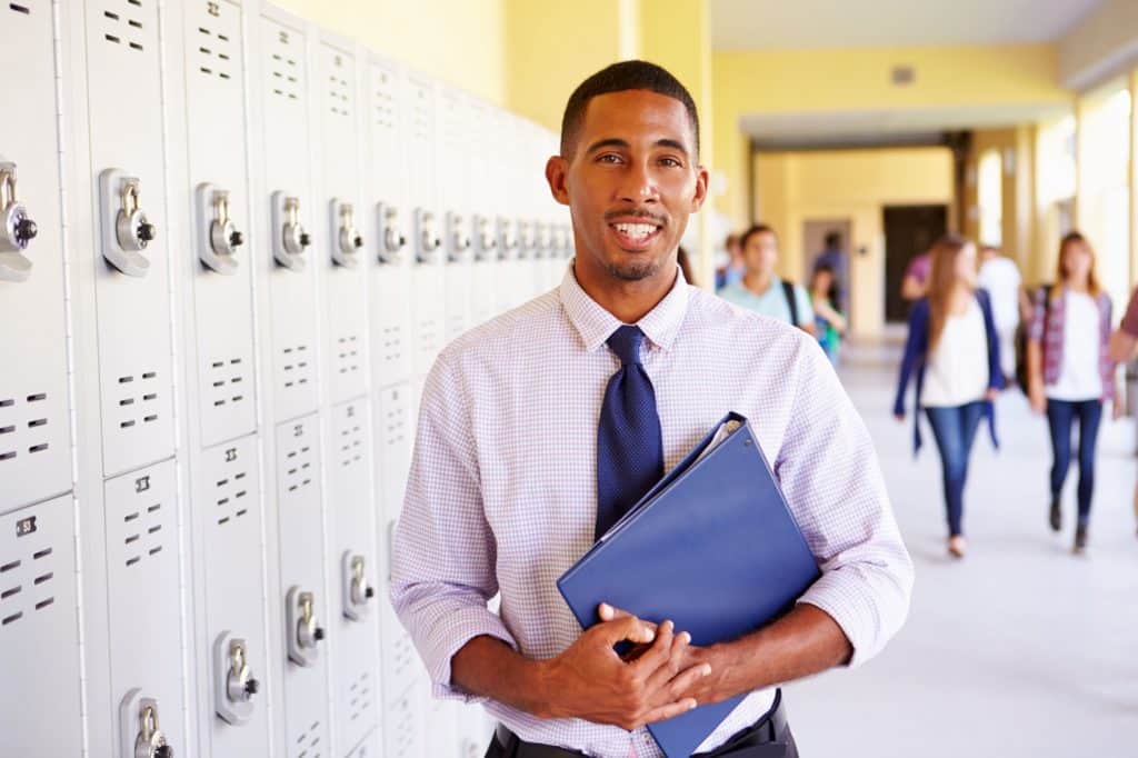 Man holding a binder standing next to lockers.