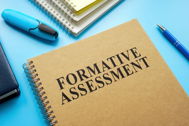 A notebook with the lettering, “formative assessments” sits on a teachers desk.