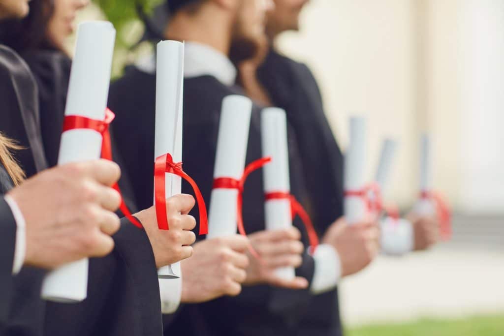 Scrolls of diplomas in the hands of a group of graduates.