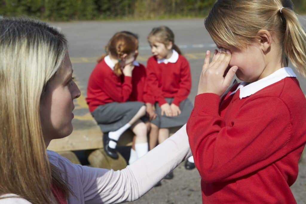 A teacher comforts her crying student on the playground.