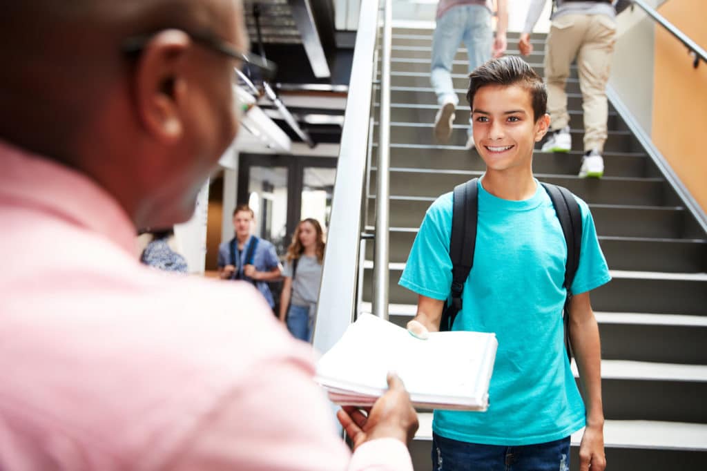 A teacher handing a smiling student papers in school.