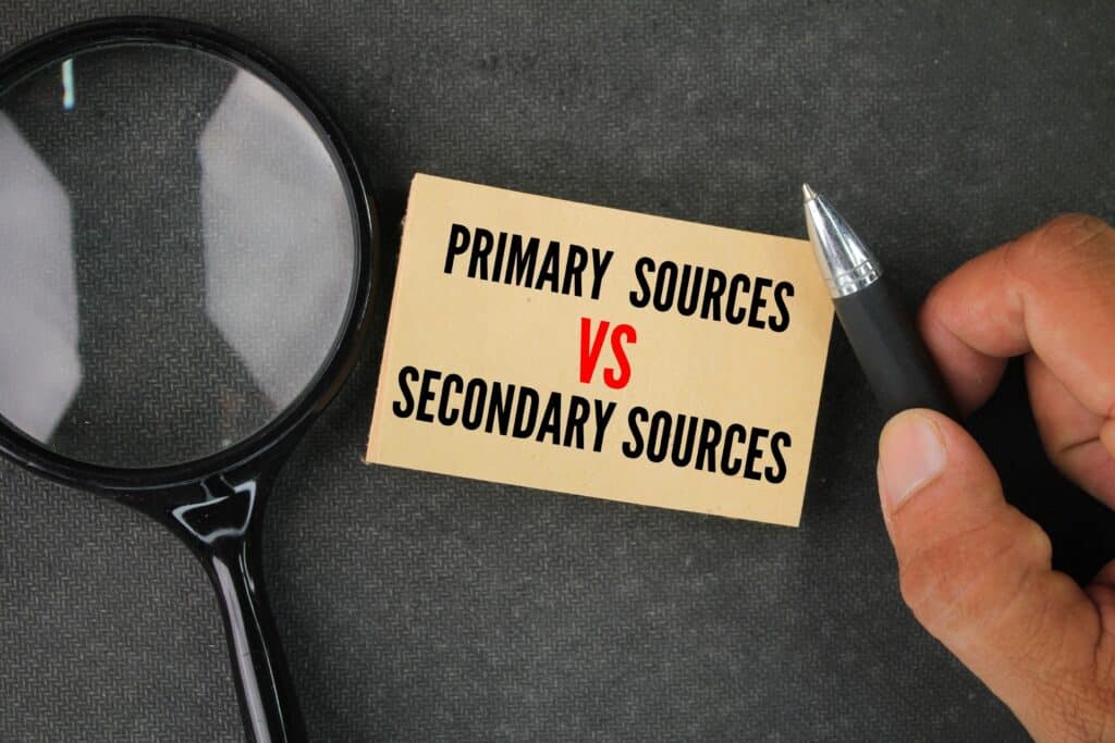 Magnifying glass next to a note that reads primary sources vs secondary sources