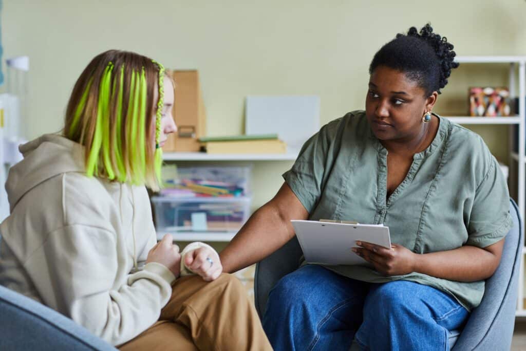 A school counselor and student sit together in an office, discussing student mental health.