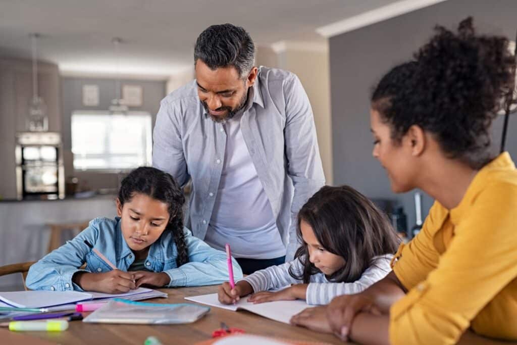 Two parents sit with their children as they do homework for elementary school.