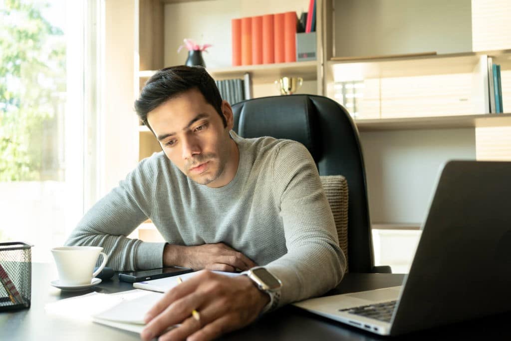 Man sitting at a desk reviewing notes and using a laptop.