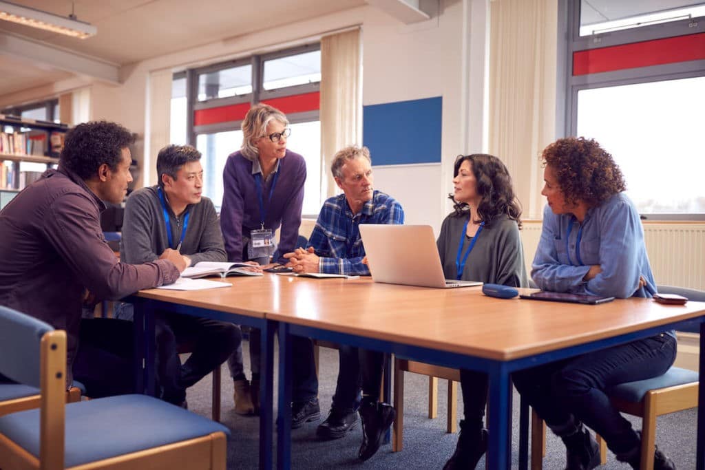 A group of teachers sits around a table and discusses with each other.