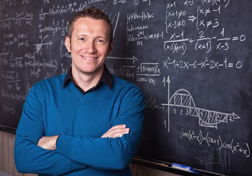 Male teacher standing in front of a blackboard filled with difficult math problems.