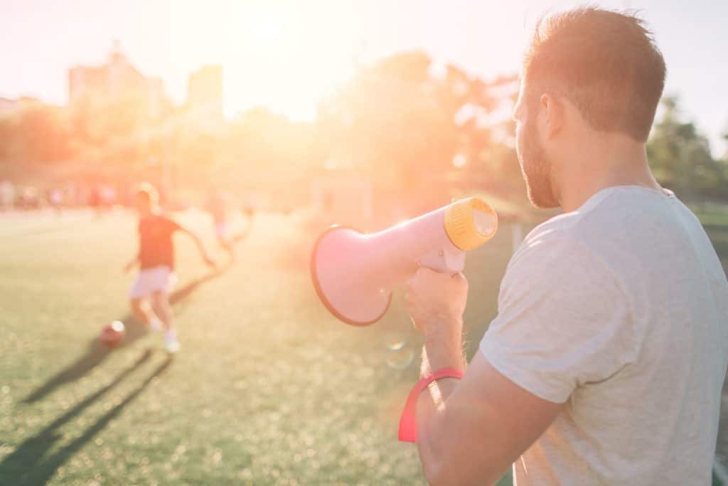The head coach, holding a megaphone, watches a soccer game.