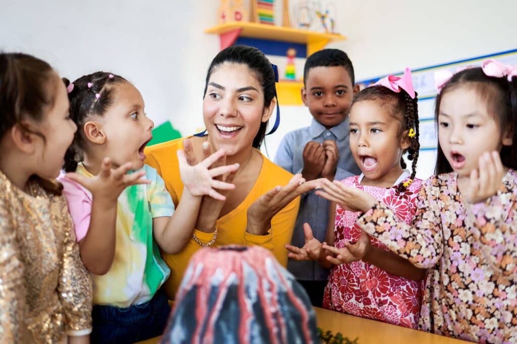 A preschool teacher sits with her students.