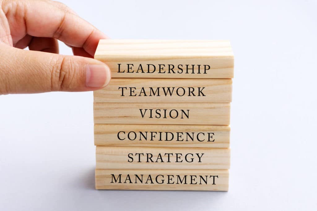 Someone touching the top block that reads ‘leadership’ on a stack of wooden blocks.