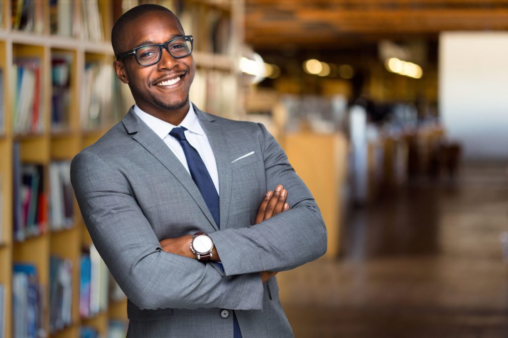Gentleman in a suit smiling while standing in a library.