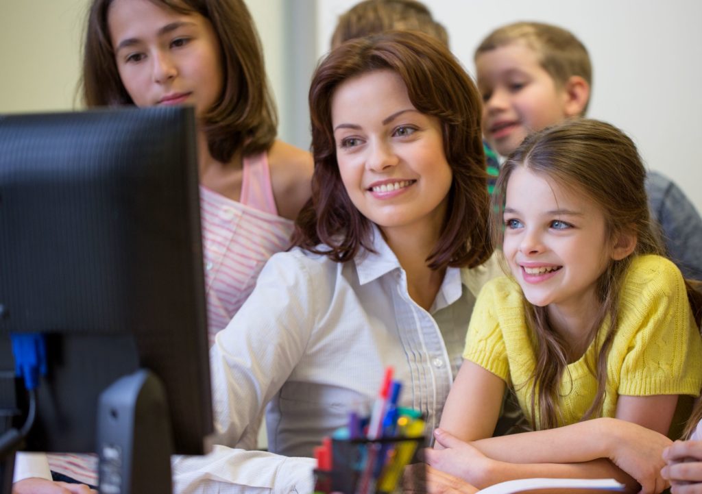 Female teacher at a computer helping a group of students.